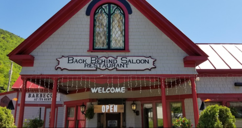 Exterior of the Back Behind Saloon Restaurant, featuring a welcoming sign and vibrant red accents against a green backdrop.