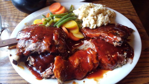 A plate of barbecue ribs with sauce, served with mashed potatoes and mixed vegetables.