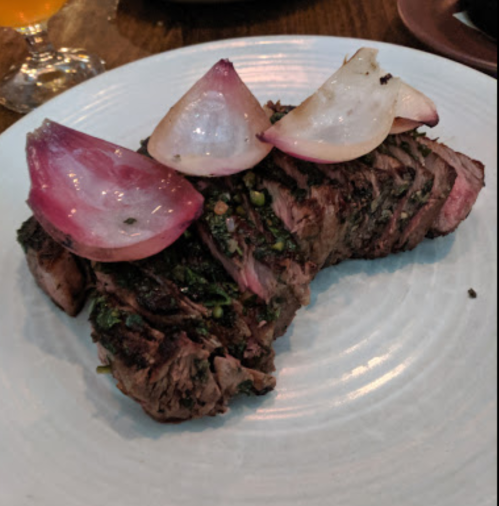 A grilled steak garnished with sliced onions, served on a white plate.