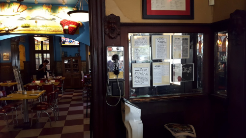 Interior of a restaurant featuring a phone booth, wall menus, and colorful decor with tables in the background.