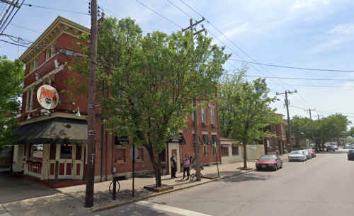 A brick building with trees outside, featuring a restaurant entrance and parked cars along the street.