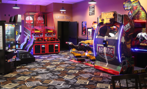 A colorful arcade room featuring various games, including basketball, racing, and a Jurassic Park-themed machine.