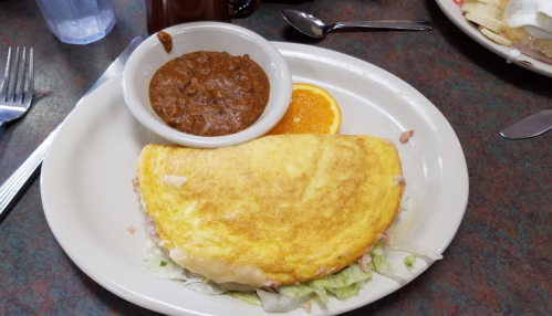 A plate with a large omelette, a side of beans, and an orange slice, served on a table with utensils.