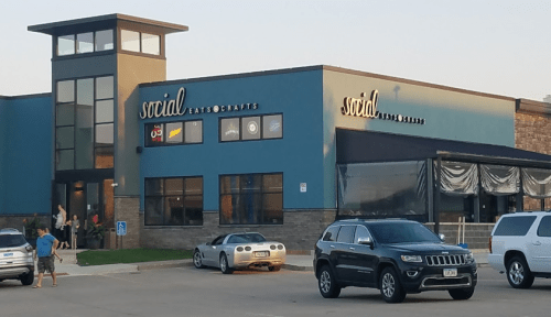 Exterior of a modern building with "social eats & crafts" signage, featuring cars parked in front and people nearby.