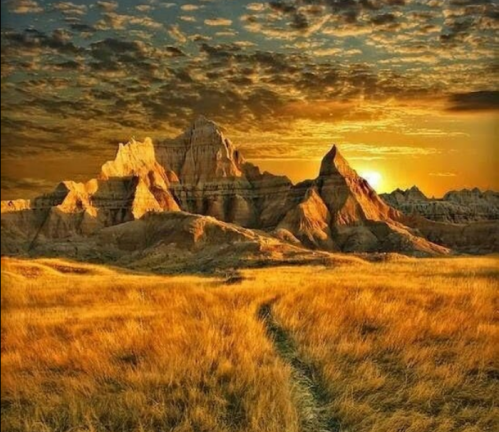 Golden sunset over rugged mountains and grassy plains, with dramatic clouds in the sky.
