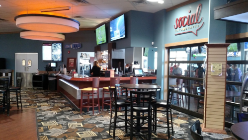 Interior of a casual dining space with a bar, seating area, and large screens displaying sports.