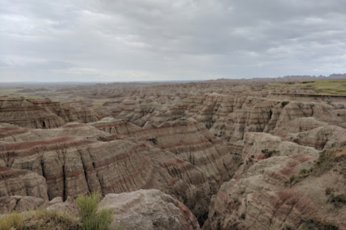 A vast, rugged landscape of layered rock formations under a cloudy sky, showcasing the beauty of a canyon.