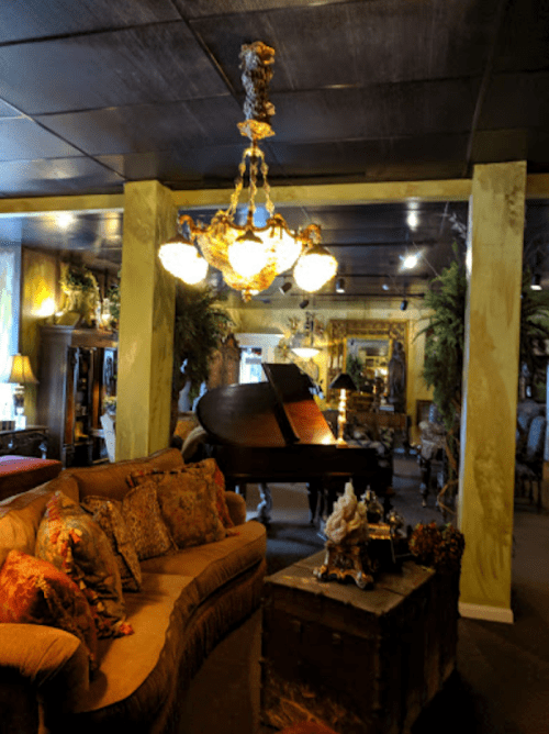 A cozy, elegantly decorated room featuring a grand piano, plush seating, and a decorative chandelier.