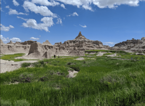 A scenic view of rugged rock formations and green grass under a blue sky with fluffy clouds.