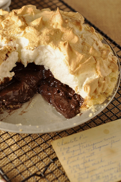 A chocolate pie with a golden meringue topping, partially sliced to reveal its rich, dark filling.
