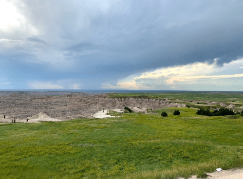 A vast landscape featuring rolling hills, grasslands, and dramatic cloud formations over a rugged terrain.