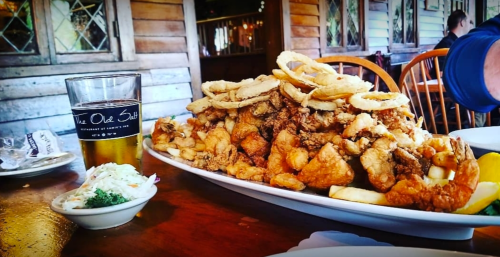 A large platter of fried seafood and onion rings, with a side of coleslaw and a glass of beer on a wooden table.