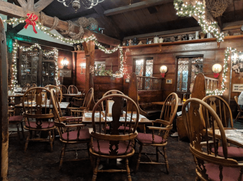 Cozy restaurant interior with wooden decor, festive lights, and empty tables and chairs.