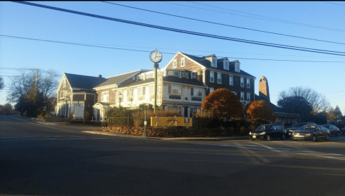 A charming hotel with a sign, surrounded by trees and parked cars, on a sunny day.