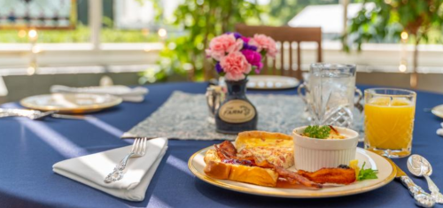 A beautifully set table with a plate of breakfast, flowers, a glass of orange juice, and a water glass.