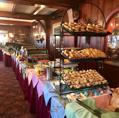 A buffet table with various pastries and dishes, decorated with colorful tablecloths and flowers in a cozy setting.