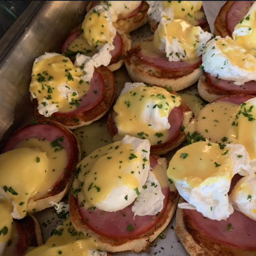 A tray of English muffins topped with ham, poached eggs, and hollandaise sauce, garnished with parsley.