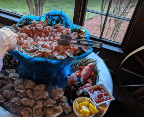 A seafood platter featuring shrimp, oysters, and lobster, garnished with lemon and cocktail sauce.