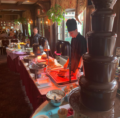 A buffet table with a chocolate fountain, food stations, and a chef serving dishes in a cozy dining room.