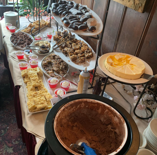 A dessert table featuring various cakes, pastries, and ice cream in bowls, set in a cozy indoor setting.