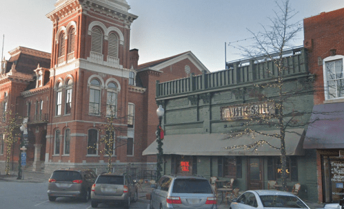 Historic buildings line a street, featuring a large brick structure and a restaurant with outdoor seating.