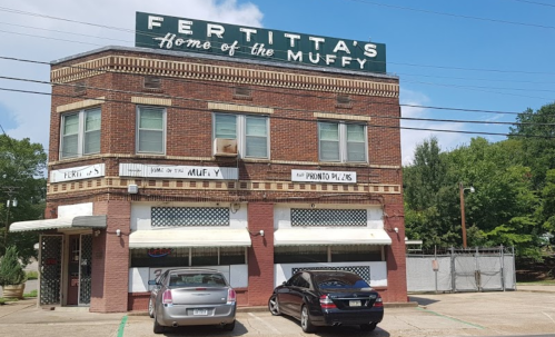 Brick building with "Fertitta's Home of the Muffy" sign, featuring parked cars and a clear blue sky.