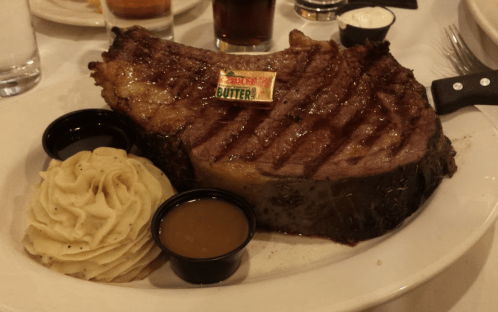 A large, grilled steak with a pat of butter on top, served with mashed potatoes and gravy on the side.