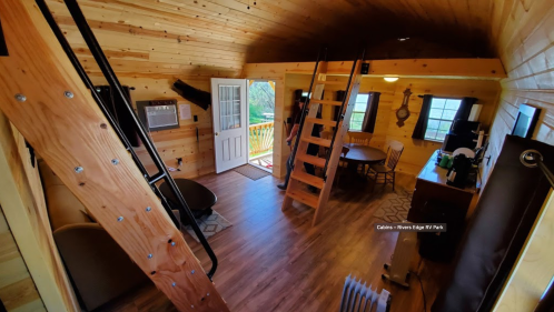 Cozy wooden interior of a cabin with a staircase, dining area, and large windows letting in natural light.
