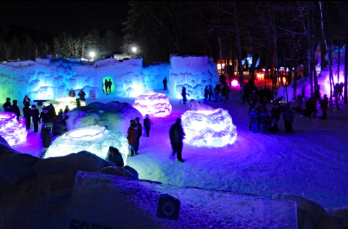 A vibrant ice sculpture park at night, illuminated with colorful lights and filled with visitors exploring the icy landscape.
