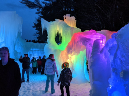 Colorful ice formations illuminated at night, with people exploring the icy landscape.