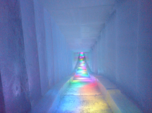 A colorful, illuminated ice tunnel with vibrant lights reflecting off the icy walls.