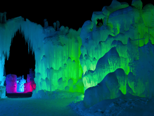 Colorful ice formations illuminated in green, blue, and pink, creating a magical winter landscape at night.