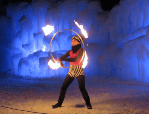 A performer twirls flaming hoops in front of a blue ice backdrop during a winter festival.