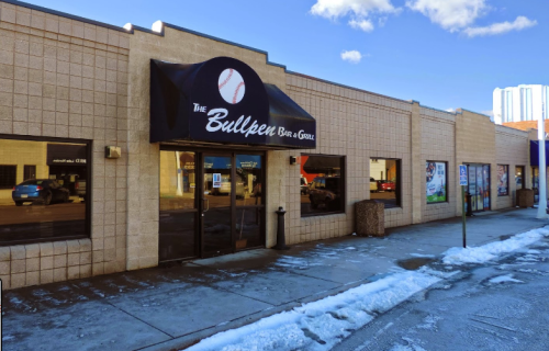 Exterior of The Bullpen Bar & Grill, featuring a baseball-themed awning and snow on the sidewalk.