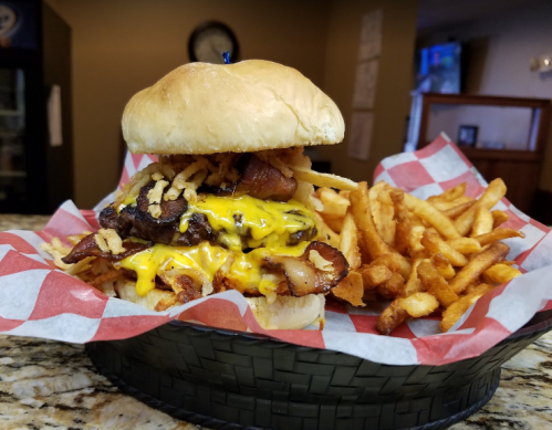 A hearty burger topped with bacon, cheese, and crispy onions, served with a side of golden French fries in a basket.