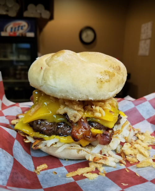 A close-up of a burger with cheese, bacon, and crispy onions on a bun, served on a checkered paper.