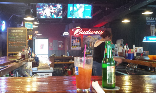 A lively bar scene with drinks on the counter, screens showing sports, and a vibrant atmosphere.