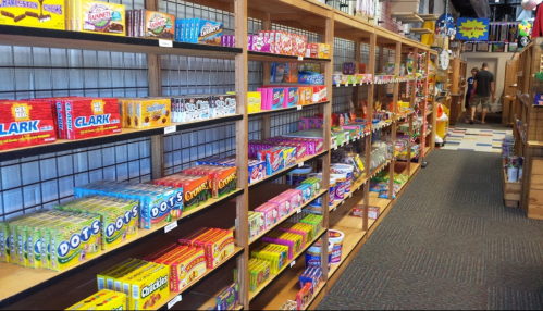 A colorful candy aisle filled with various sweets and snacks on wooden shelves in a store.
