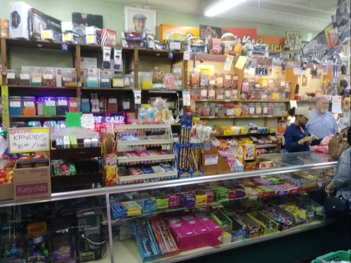 A colorful convenience store filled with snacks, candy, and various products, with customers at the counter.
