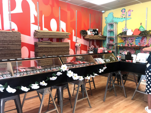 Colorful shop interior with display cases, shelves of products, and decorative elements, featuring a vibrant red wall.