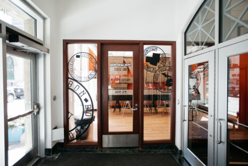 Entrance to a modern office space with large glass doors and decorative window designs. Bright interior visible.