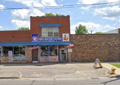 A brick storefront with a blue awning, featuring a candy and ice cream shop, decorated with American flags.
