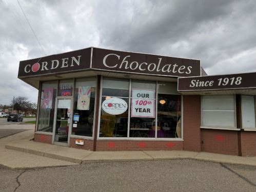 Exterior of Corden Chocolates store, featuring a sign celebrating its 100th year, with an "Open" banner.