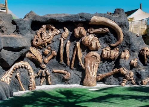 A textured wall featuring large, sculpted dinosaur bones and fossils against a blue sky backdrop.