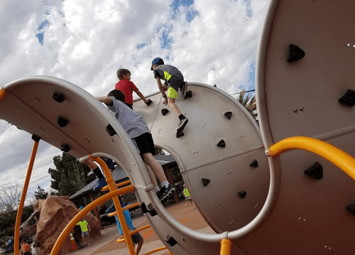 Three children climb on a playground structure under a cloudy sky, enjoying their time outdoors.