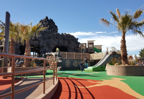 A colorful playground with palm trees, rock formations, and a slide under a clear blue sky.