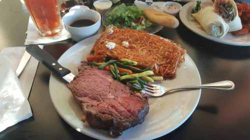 A plate featuring a juicy slice of prime rib, stir-fried vegetables, and a serving of fried noodles.
