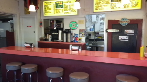 A diner counter with stools, a menu board, a clock, and a drink station in the background.