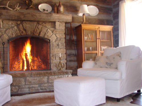 Cozy living room with a stone fireplace, white armchair, and wooden cabinet, creating a warm, inviting atmosphere.
