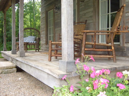 A rustic porch with wooden rocking chairs and colorful flowers in the foreground, surrounded by greenery.
